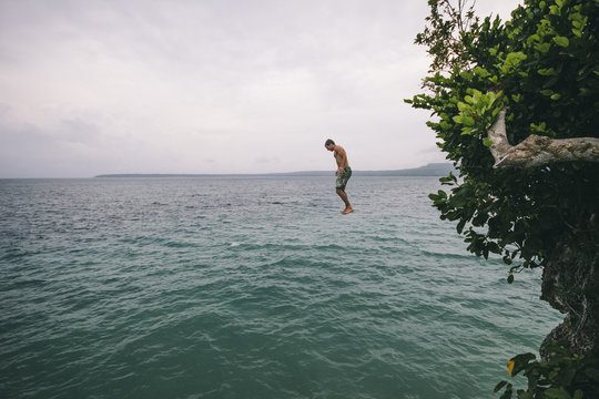 Young man jumping off a cliff into the sea