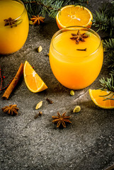 Fall, winter cocktails, Hot spicy winter orange punch with cinnamon, anise stars, cardamom, cloves. On black stone table, with ingredients and christmas tree branches, in glasses. Copy space