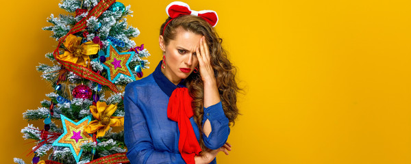 stressed woman near Christmas tree isolated on yellow background