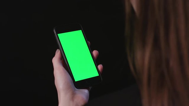 Young Woman is Holding Phone with green Screen at studio with black Bbackground, scroll down