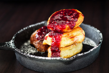 Stack homemade fried Pancakes with Raspberry jam in small cast-iron frying pan. Dark wood background. Breakfast concept.