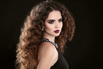 Hairstyle. Fashion brunette girl with Long curly hair, beauty makeup. Glamour portrait of beautiful woman with marsala matte lips isolated on black background.
