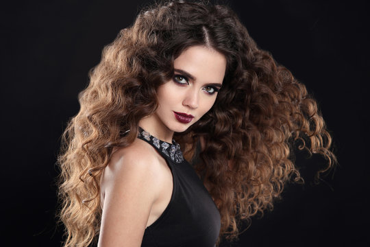 Beauty girl hair. Curly hairstyle. brunette girl with healthy long hair, beauty makeup. Beautiful woman with marsala matte lips, blowing hairstyle isolated on black background