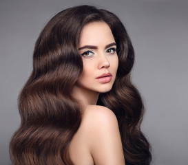 Naklejka premium Beauty hair. Brunette girl portrait with long shiny wavy hair. Beautiful model with healthy hairstyle and clean makeup isolated on studio dark background. Shampoo care product.