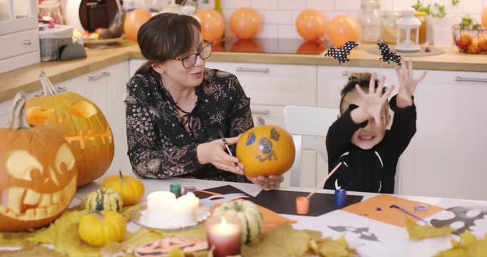 Woman in glasses holding pumpkin with painted face and little girl in cute Halloween costume trying to be scary.