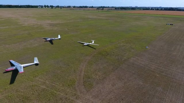 Aerial shooting of three glider planes in an even green field in a sunny day