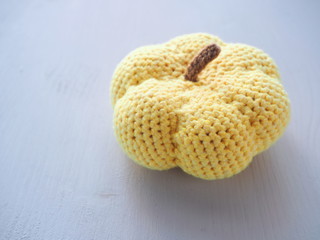 Crochet pumpkin upon white wooden table close up. Halloween decoration. Selective focus. Copy space for your text.