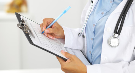 Close-up of a female doctor filling  up medical form at clipboard while standing straight in hospital