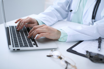 Close-up of a female doctor typing on laptop computer, sitting at the table in the hospital