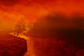 Fog of mist hovering over a small, winding river lit by red, morning sun