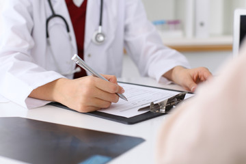 Fototapeta premium Close up of a female doctor filling up an application form while consulting patient