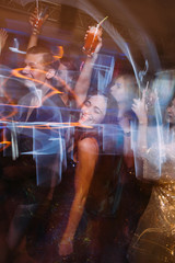 Happy party with alcohol at night club in blurred motion. Joyful friends at Christmas discotheque,...