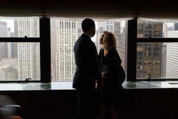 Man stands before a stunning woman looking through the panoramic window at New York streets