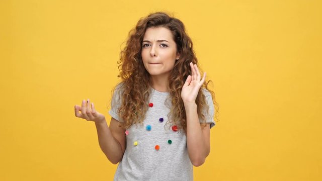 Young curly woman in t-shirt does not hear something over yellow background