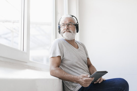 Mature man with tablet and headphones looking out of window
