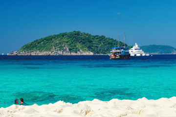 View from the beach to the crystal blue water of the Andaman Sea and Similan Island, Thailand. Loving couple bathes in water, tropical paradise. Selective focus