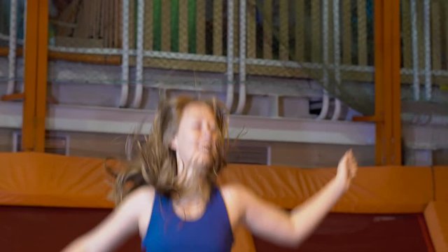 Young woman sportsman jumping on a trampoline in fitness park and doing exersice indoors