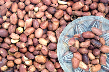 Fried peanuts in small glass bowl and lot of roasted peanut fruits as background  top view closeup
