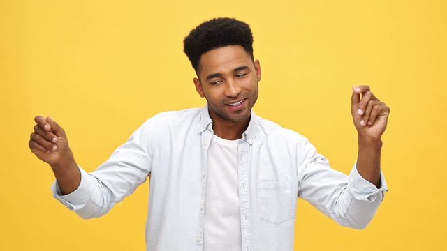 Happy african man in shirt dancing and looking at the camera over yellow background