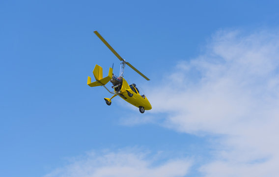 Yellow gyrocopter in air on blue sky and clouds