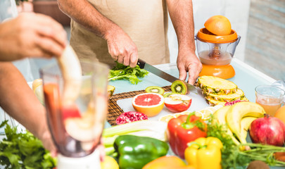 Detail of senior couple in kitchen with healthy food - Retired people cooking at home preparing blended centrifuge smoothie with bio fruit and vegetables - Happy elderly concept with mature pensioner