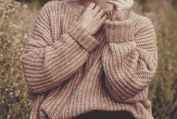 Closeup of woman wearing a beige soft oversized knitted sweater or jumper outdoors in the nature....