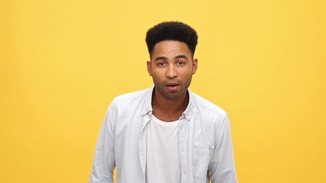 Calm african man in shirt looking at the camera and frightened after that over yellow background