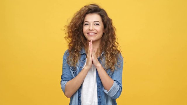 Happy shocked curly woman in denim shirt rejoice and clapping over yellow background