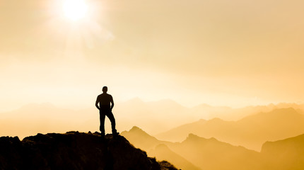 Man reaching summit enjoying freedom and watching towards mountain ranges.