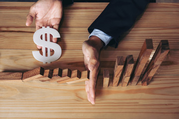 Close up of businessman hand Stopping Falling wooden Dominoes effect from continuous toppled or...