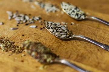 Close up of silver spoons with seeds, chopped linseed, peeled sunflower and sesame on wooden table. Concept of healthy eating.
