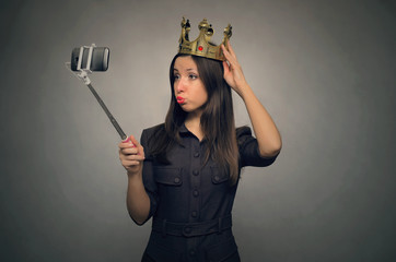 Young caucasian girl with golden crown above her head makes selfie photo on mobile phone by using...