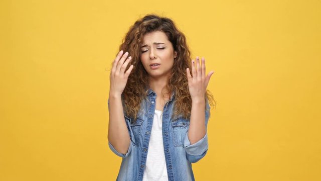 Upset curly woman in denim shirt looking at camera over yellow background