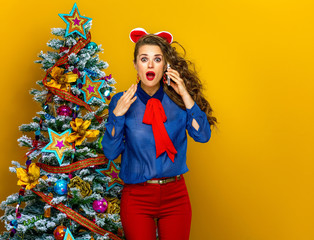 woman near Christmas tree on yellow background using cell phone