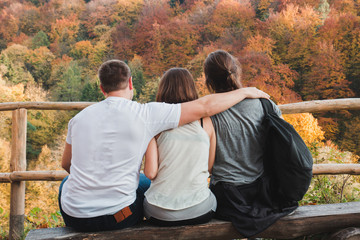 One guy hugs two girls looking at the autumn landscape