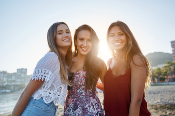 Fototapeta na wymiar Three pretty girls standing on beach in sunlight