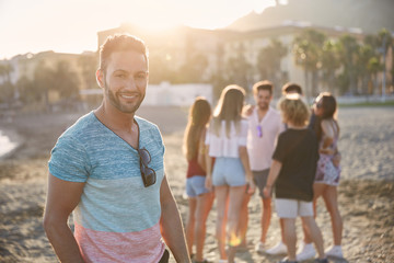 Handsome man standing on beach with his friends smiling