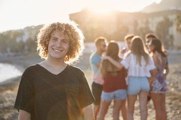 Man with curly hair standing on beach with his friends smiling