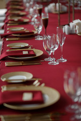 Golden knives and forks lie by golden plates on dinner table covered with red cloth