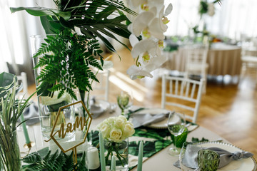 Centerpieces made of large green leaves and white flowers stand on dinner tables in the restaurant