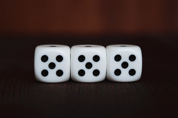 Three white plastic dices in a row on brown wooden board background. Six sides cube with black dots. Lucky number 555.