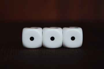 Three white plastic dices in a row on brown wooden board background. Six sides cube with black dots. Number 111.