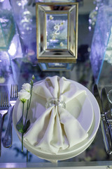 White napkin lies on white dinner plate on mirror table