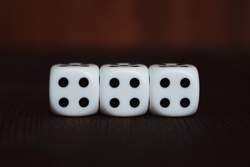 Three white plastic dices in a row on brown wooden board background. Six sides cube with black dots. Tetraphobia unlucky number 4.