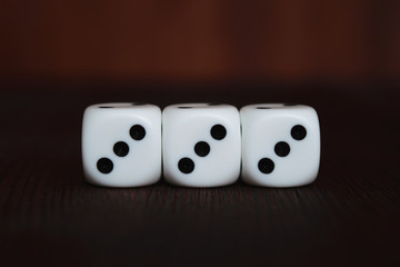 Three white plastic dices in a row on brown wooden board background. Six sides cube with black dots. Number 333.