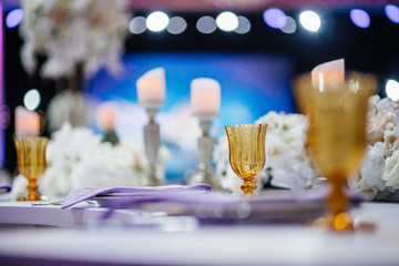 Golden glasses stand by plates with violet napkins on the table