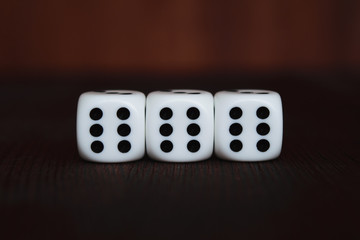 Three white plastic dices in a row on brown wooden board background. Six sides cube with black dots. Satan number 666.