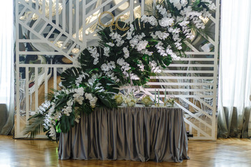 Dinner table for newlyweds decorated with large garland made of green leaves and orchids