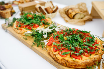 Pizza with many tomatoes and greenery served on wooden board