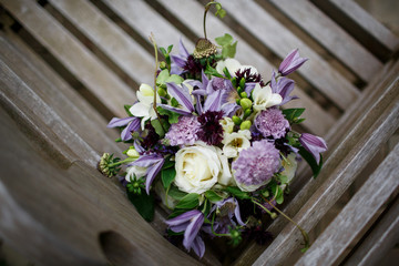 Wedding bouquet made of white and violet flowers stands on grey wooden bench